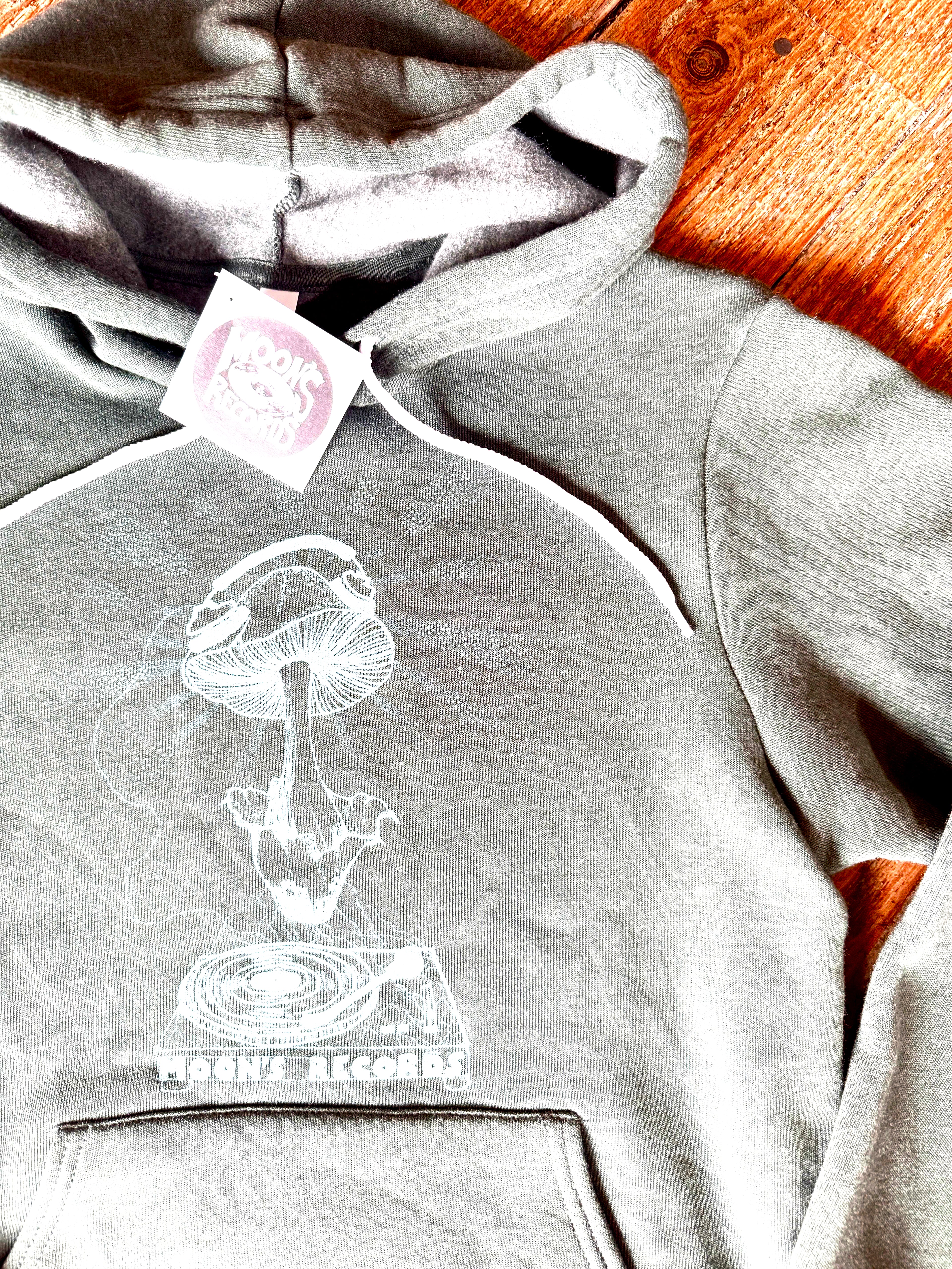 Gray hoodie with a mushroom and record design, branded 'Mushroom Records', on a wooden surface.