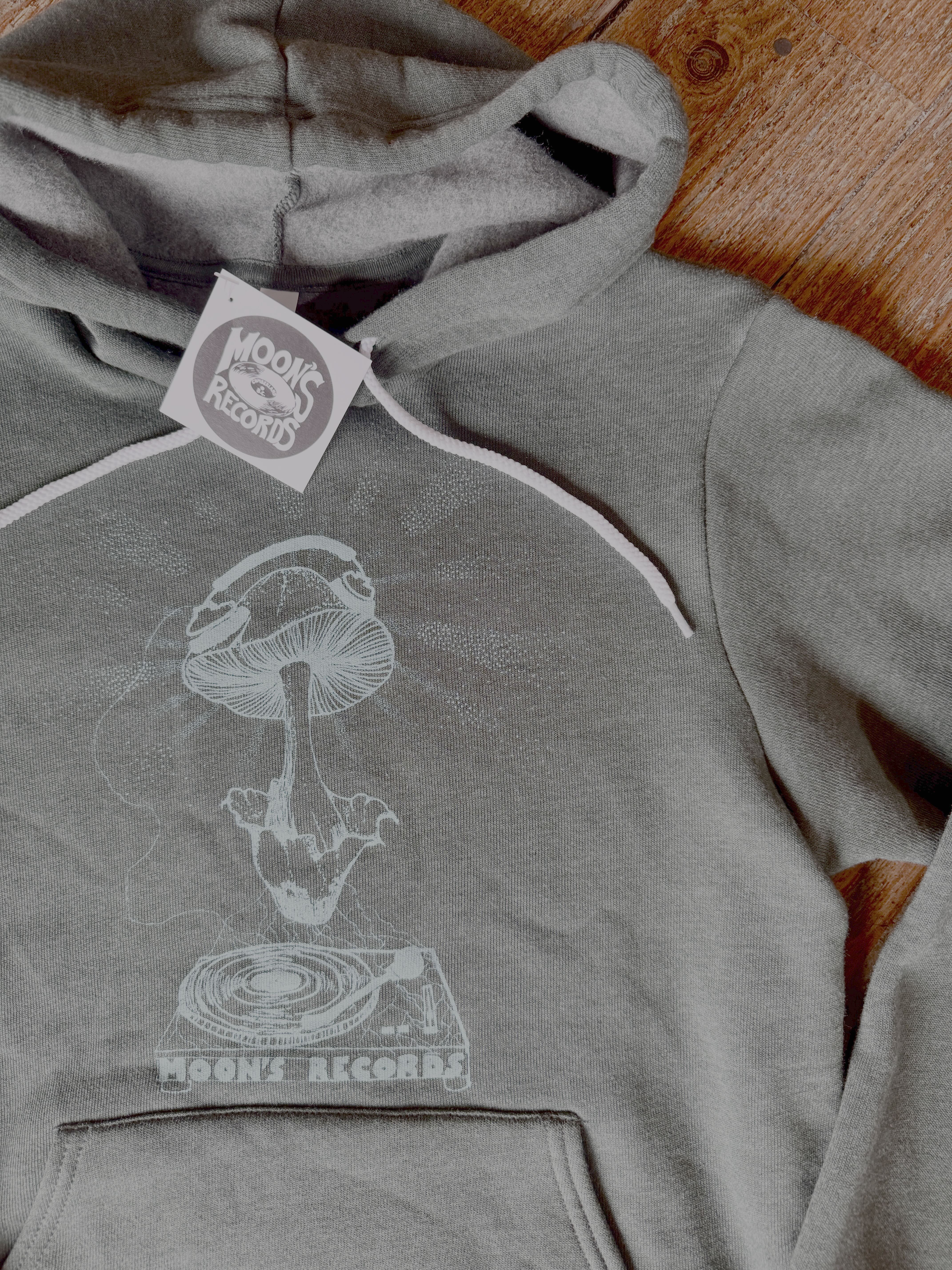 Gray hoodie with a mushroom and record design, branded 'Mushroom Records', on a wooden surface.